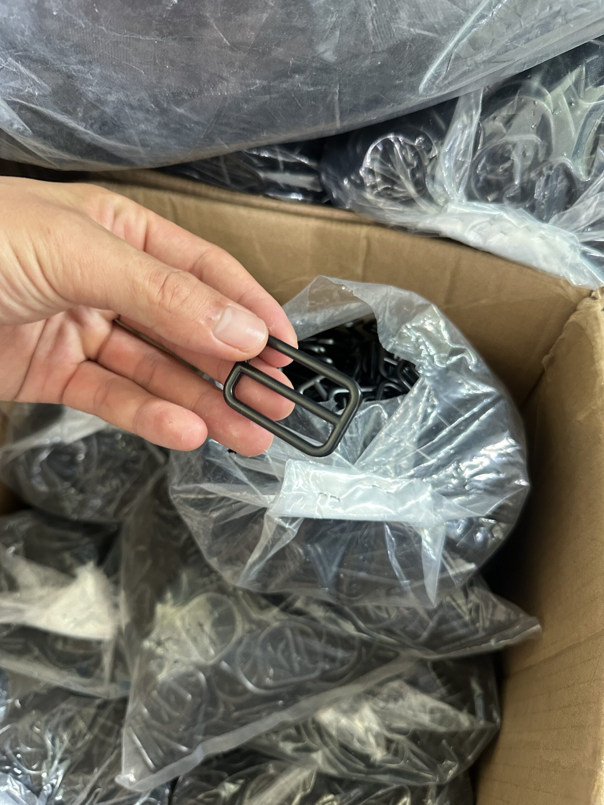 Hand holding a black metal tri-glide slider taken from a bag of hardware in a carton