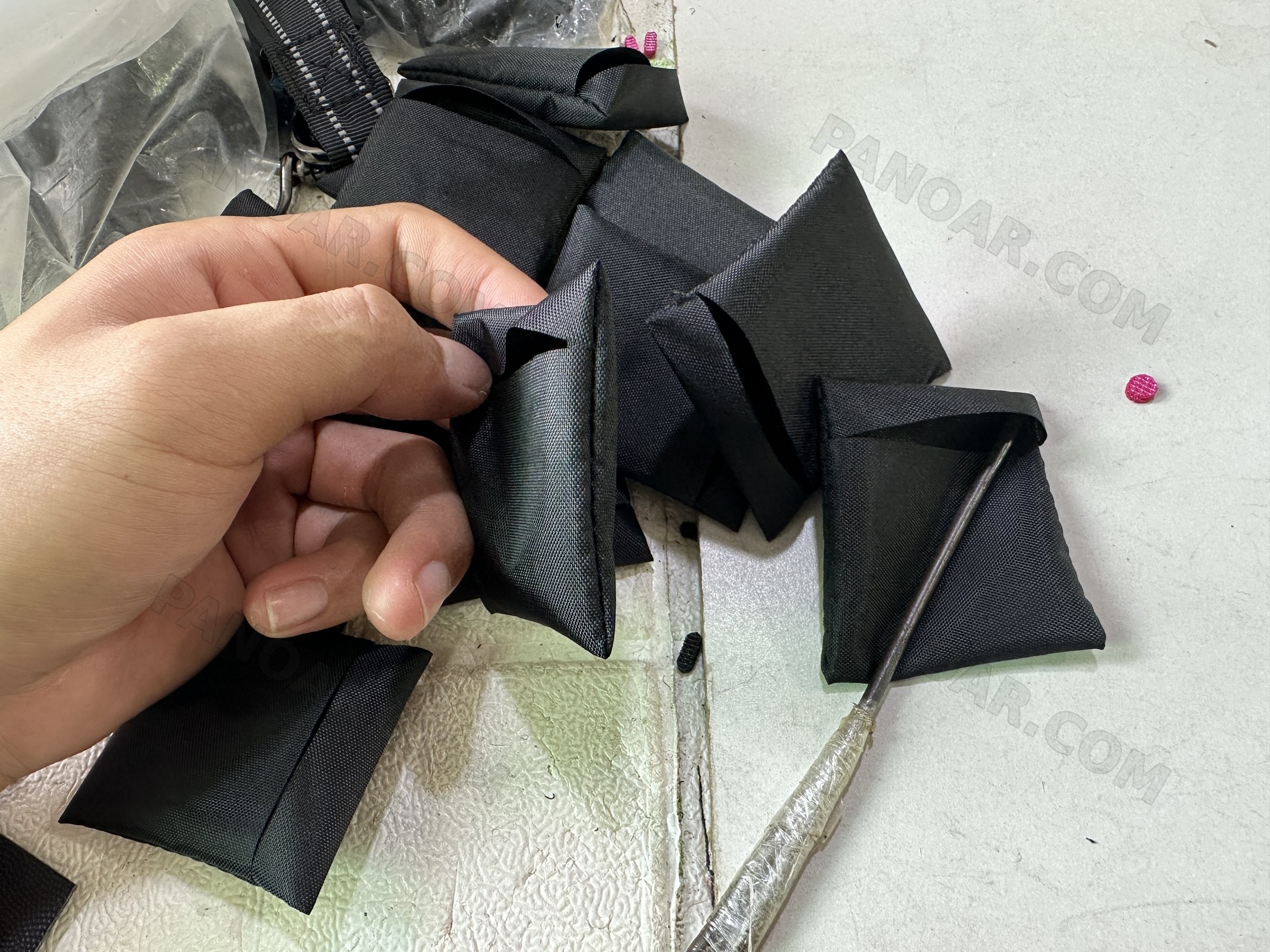 Hand holding folded black fabric parts on a work table with an awl
