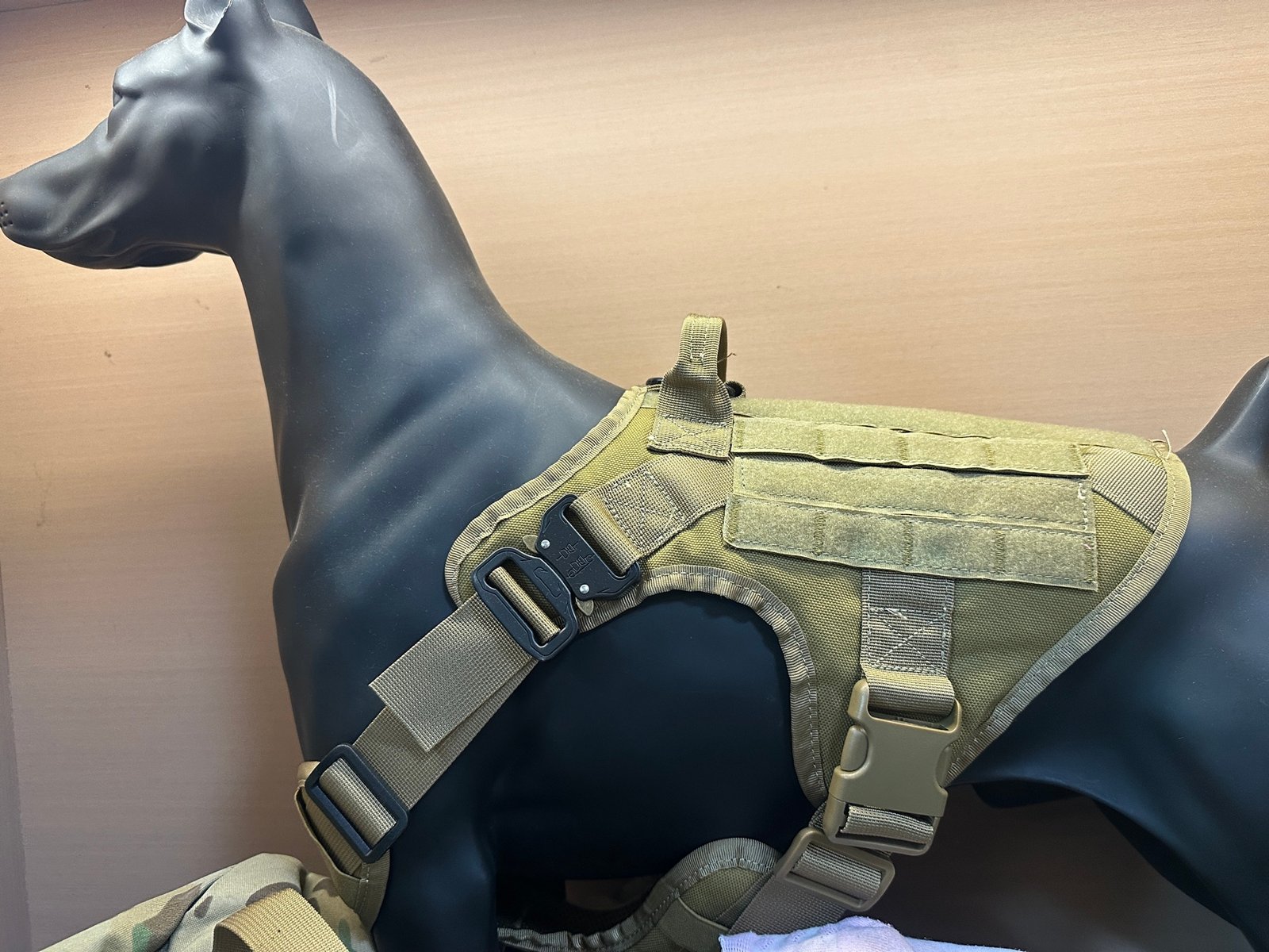Tactical dog harness reference on display model with webbing, quick-release buckle, and hook-and-loop panel