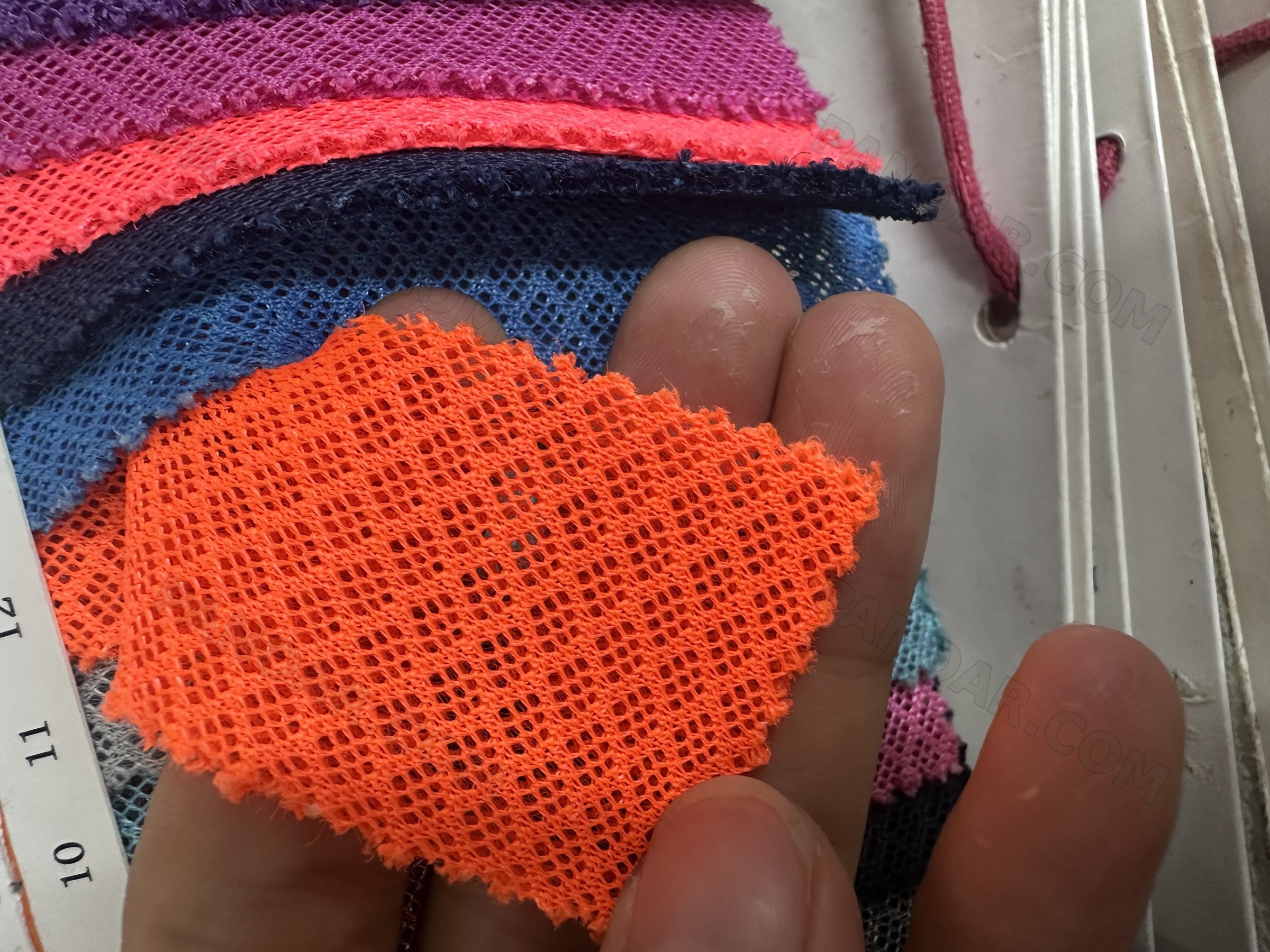 Hand holding orange mesh fabric in front of multicolor mesh swatches