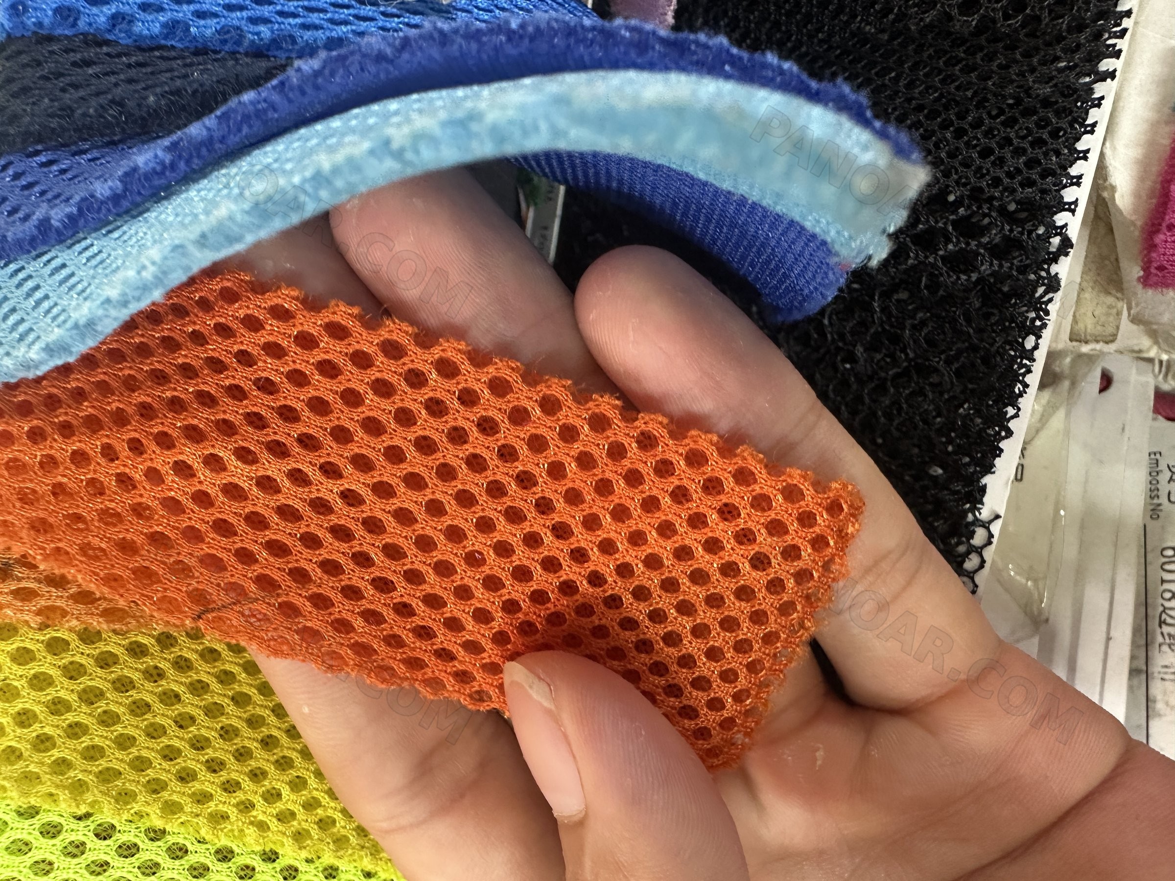Close-up of orange mesh fabric held over other mesh swatches