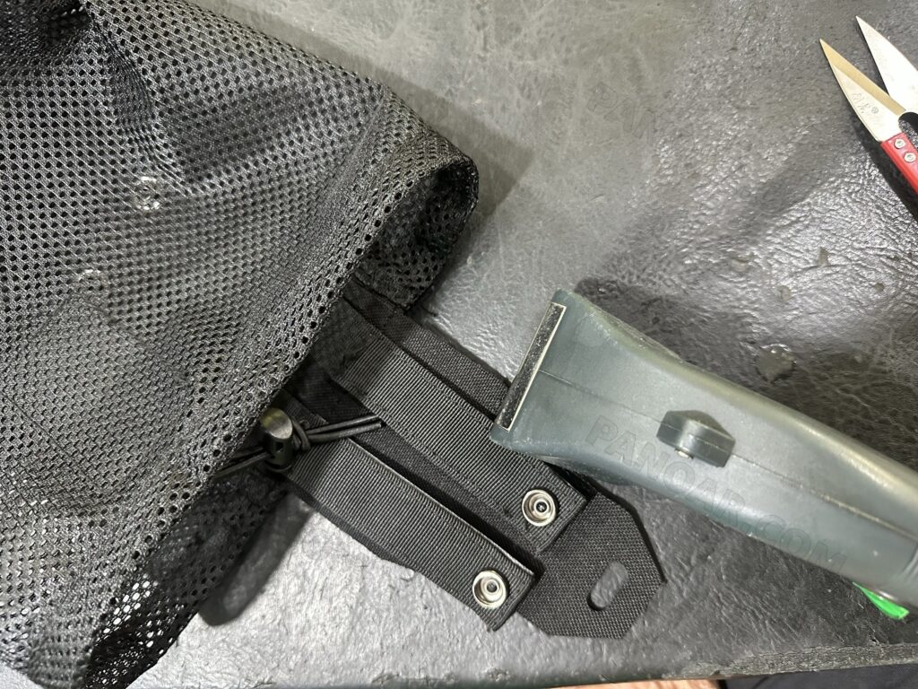 Black mesh component beside snap hardware and a hand tool