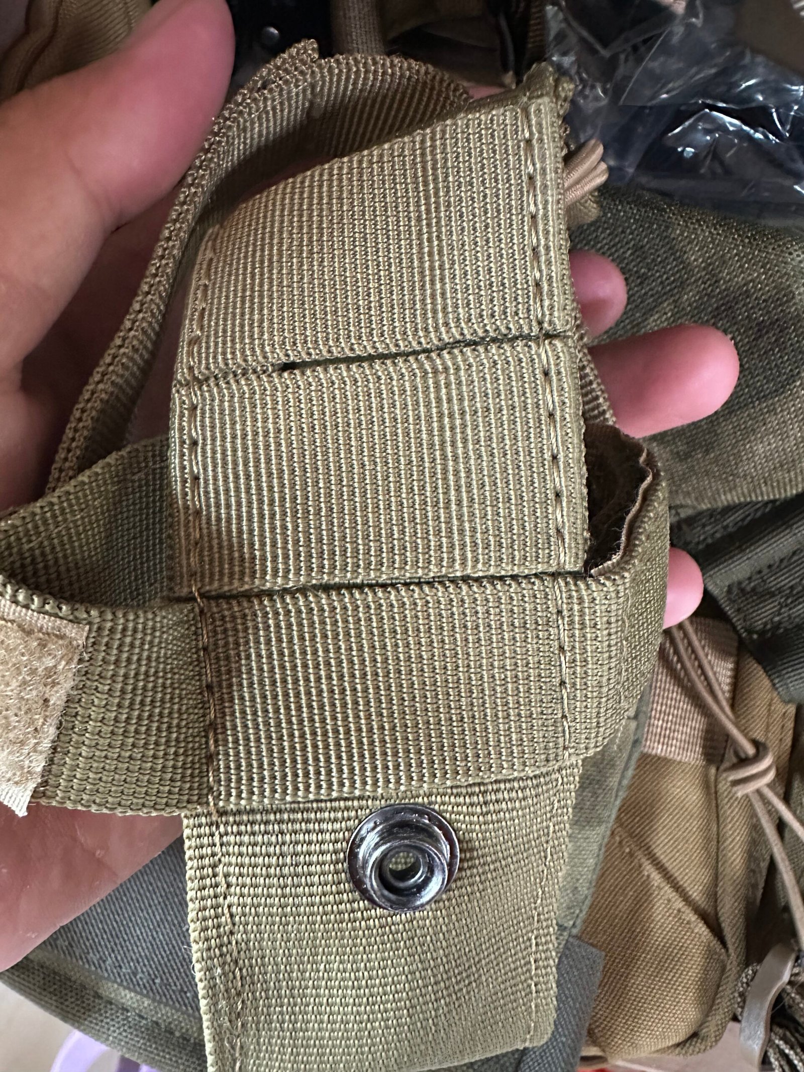Close-up of an olive green MOLLE webbing attachment strap with a snap fastener on a tactical pouch