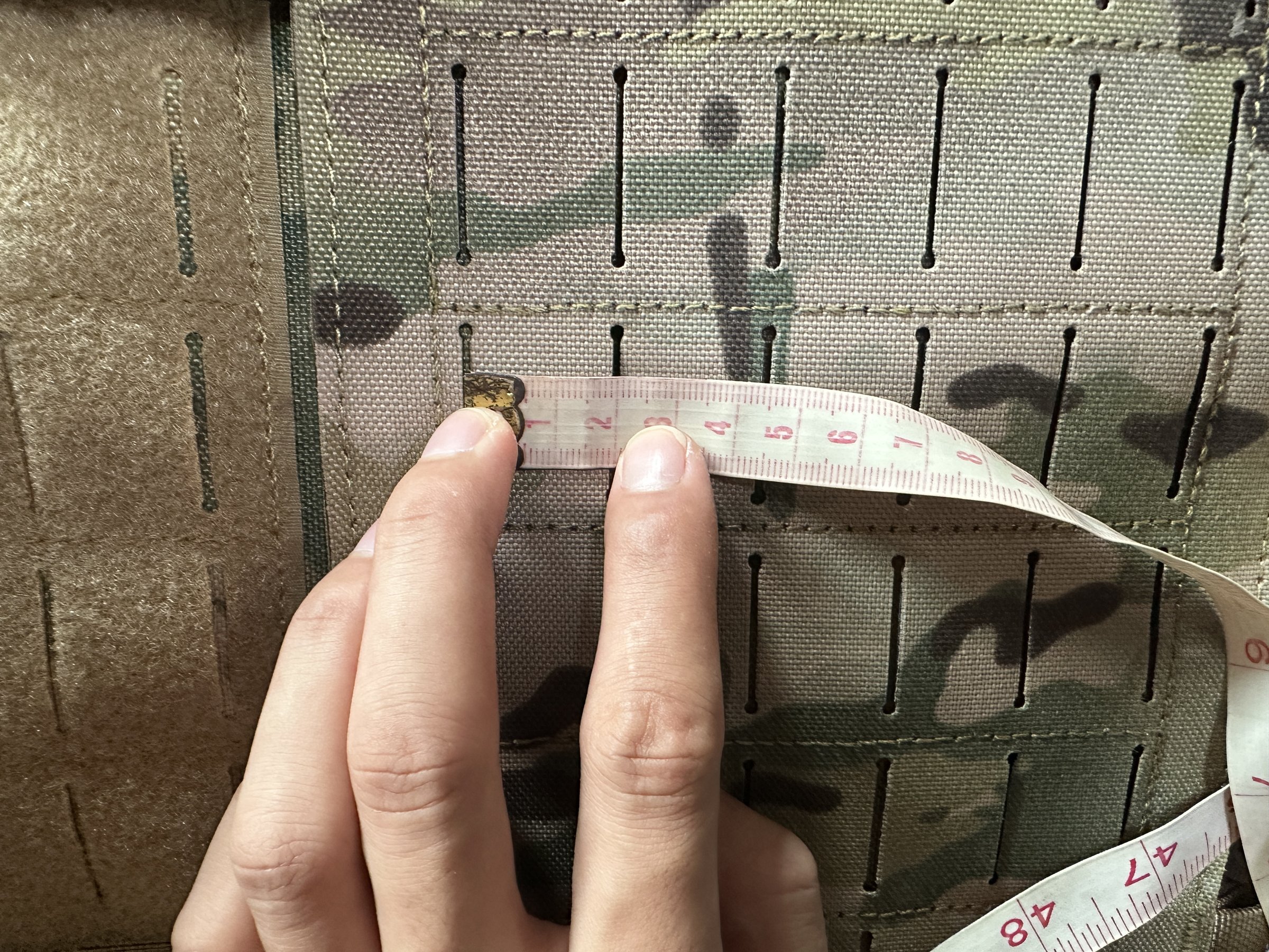 Tape measure checking MOLLE row spacing on a plate carrier panel