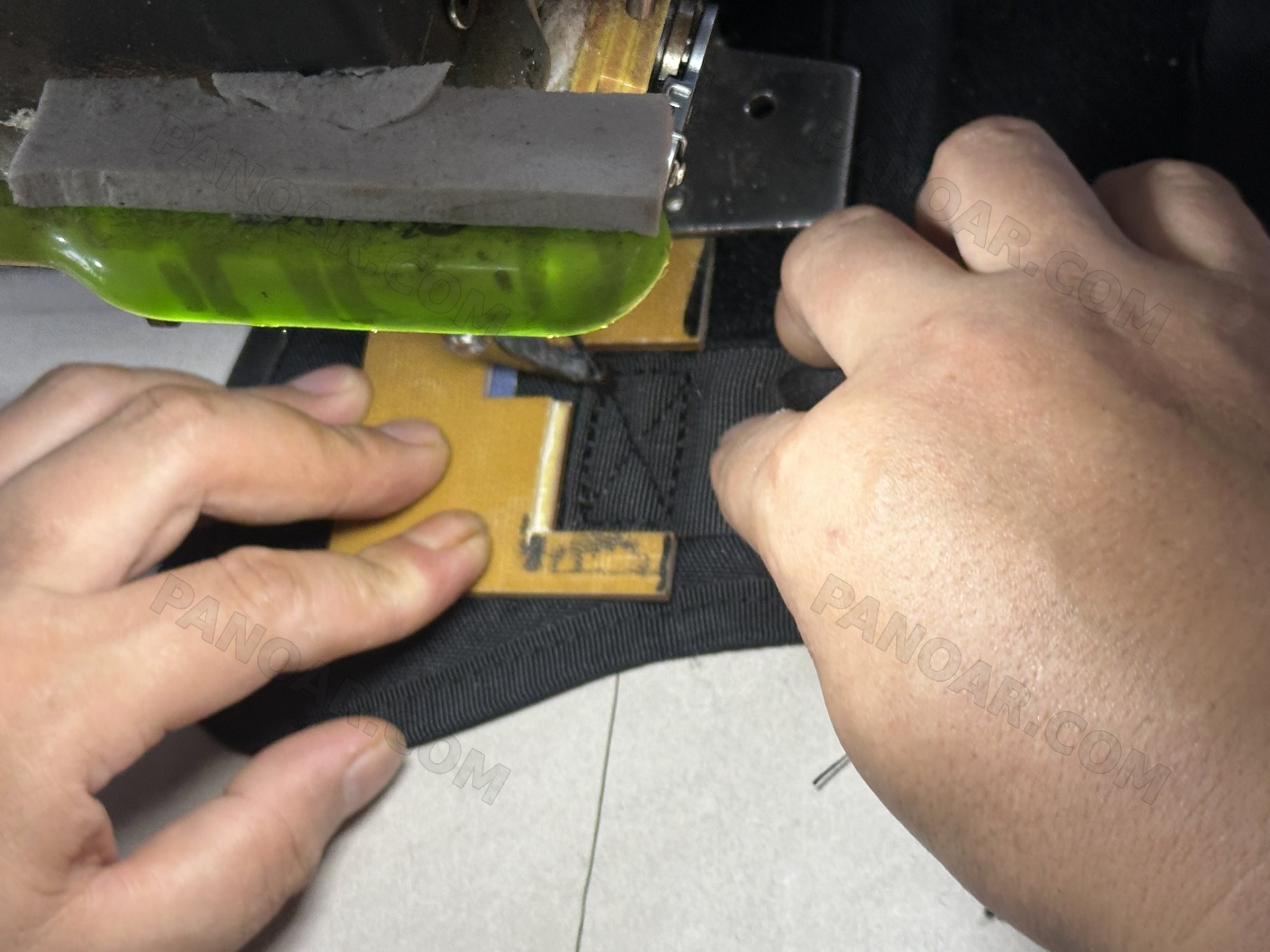 Hands positioning black fabric under a yellow template at a sewing station