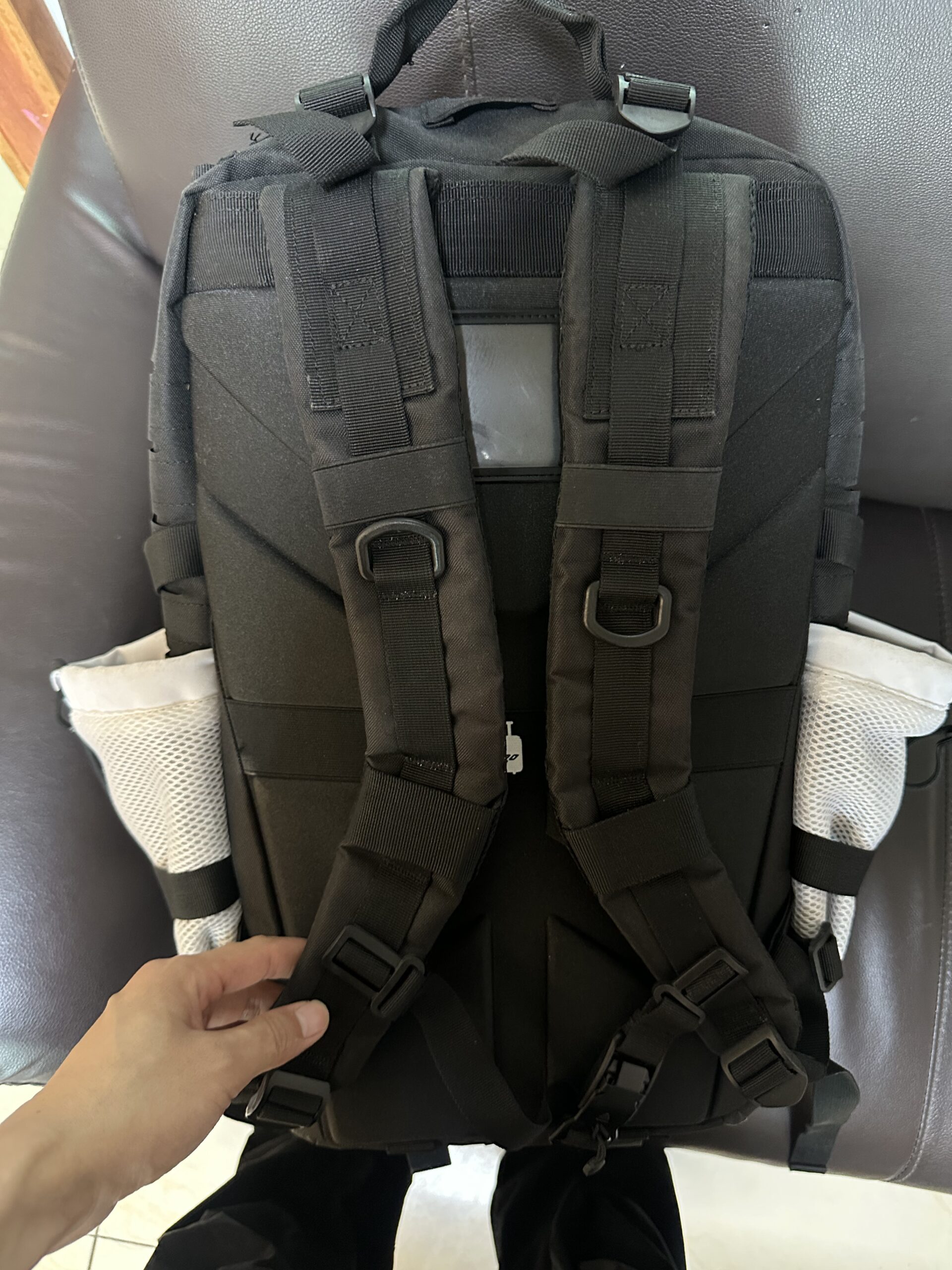 Rear view of a black tactical backpack showing padded shoulder straps, sternum strap, and mesh side pockets