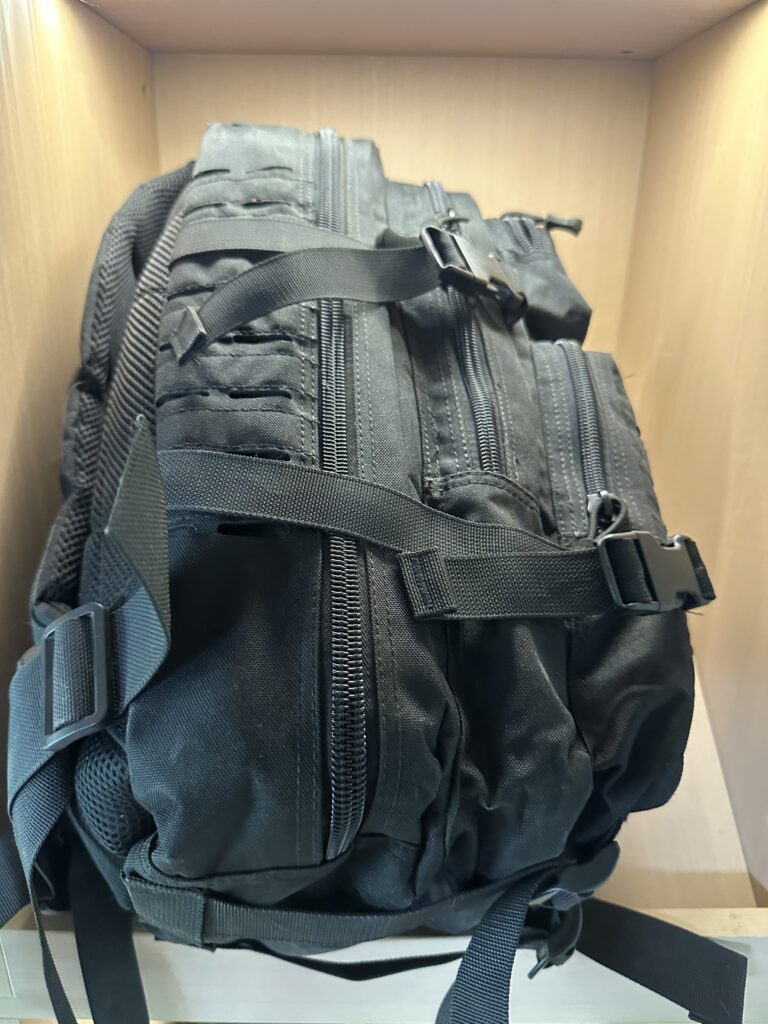Black tactical MOLLE backpack side view showing zippered compartments, MOLLE webbing, and quick-release buckles