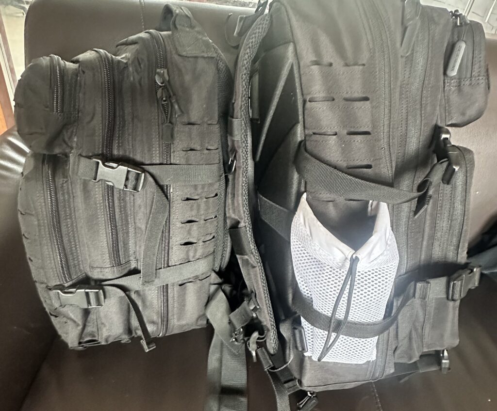 Two black tactical backpacks side by side, one featuring a white mesh side pocket, showing MOLLE webbing and strap details