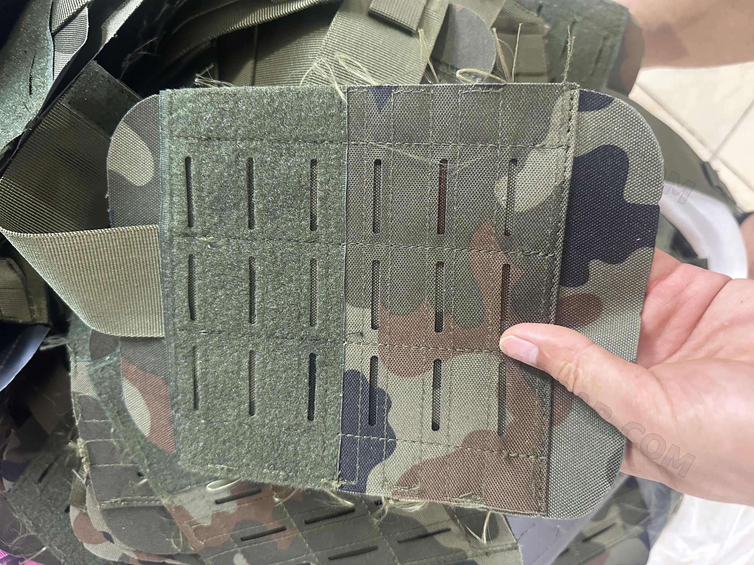 Hand holding a woodland camouflage panel with laser-cut slots and a hook-and-loop area, loose threads still untrimmed