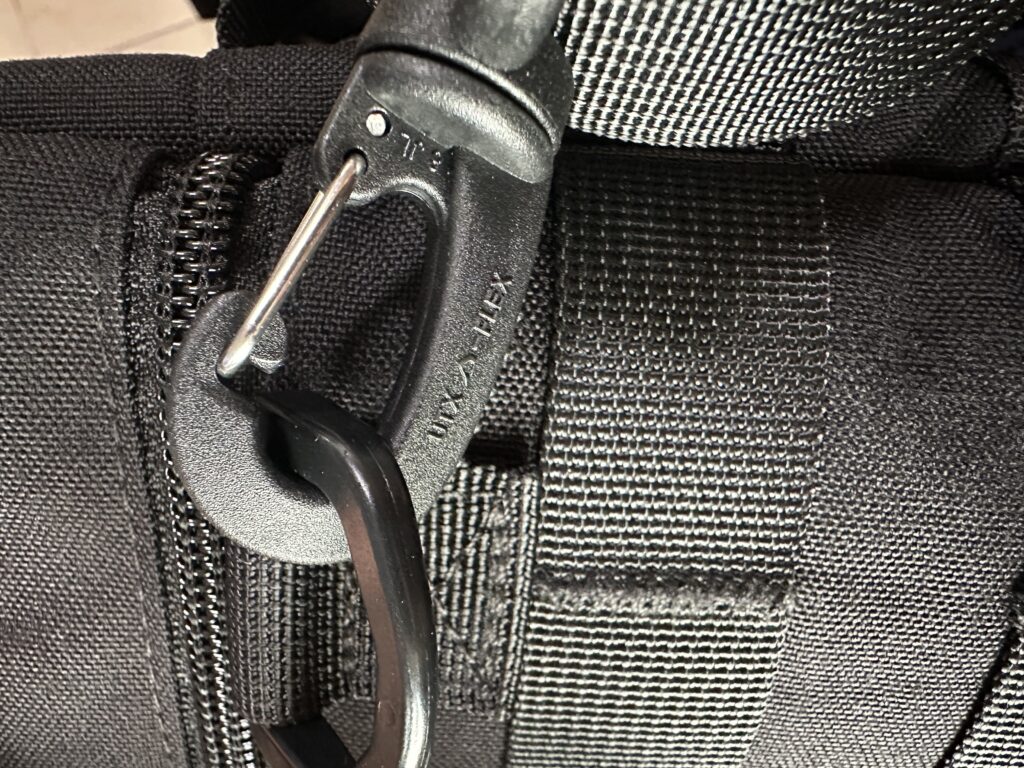 Close-up of a black hook attached to a woven webbing loop beside a zipper.