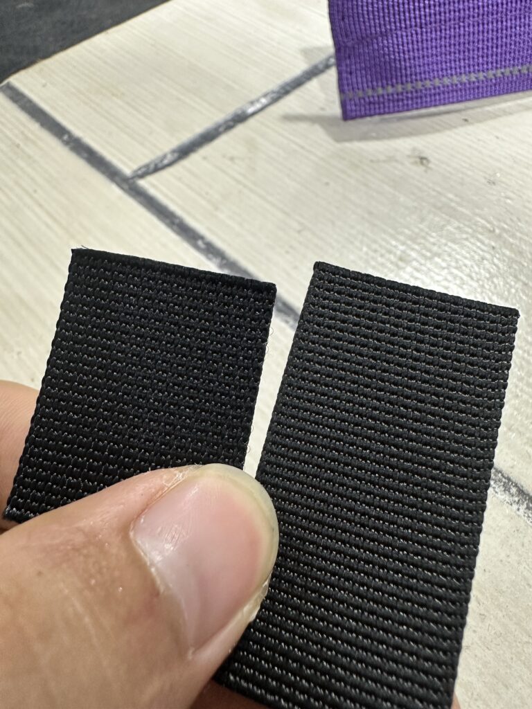 Hand holding two black webbing samples with visible woven texture