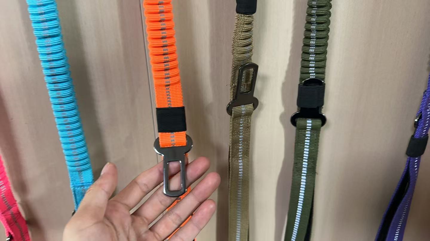 Metal vehicle seat-belt tongue attached to an orange dog leash sample.